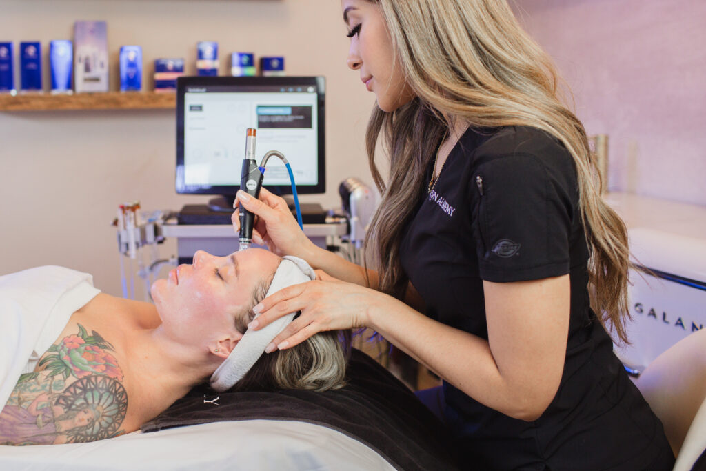 A skincare professional performing a facial treatment on a client using advanced technology at Skyn Alchemy.