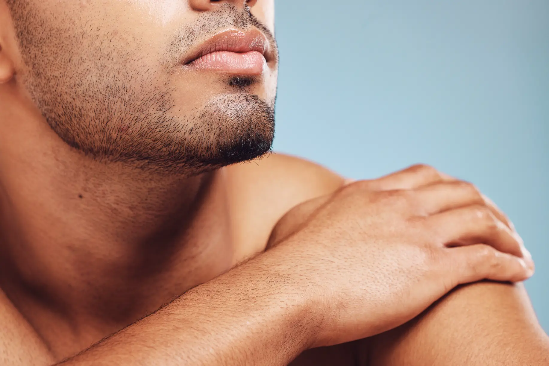 Close-up of a man’s lower face showing lips, beard stubble, and hand resting on shoulder