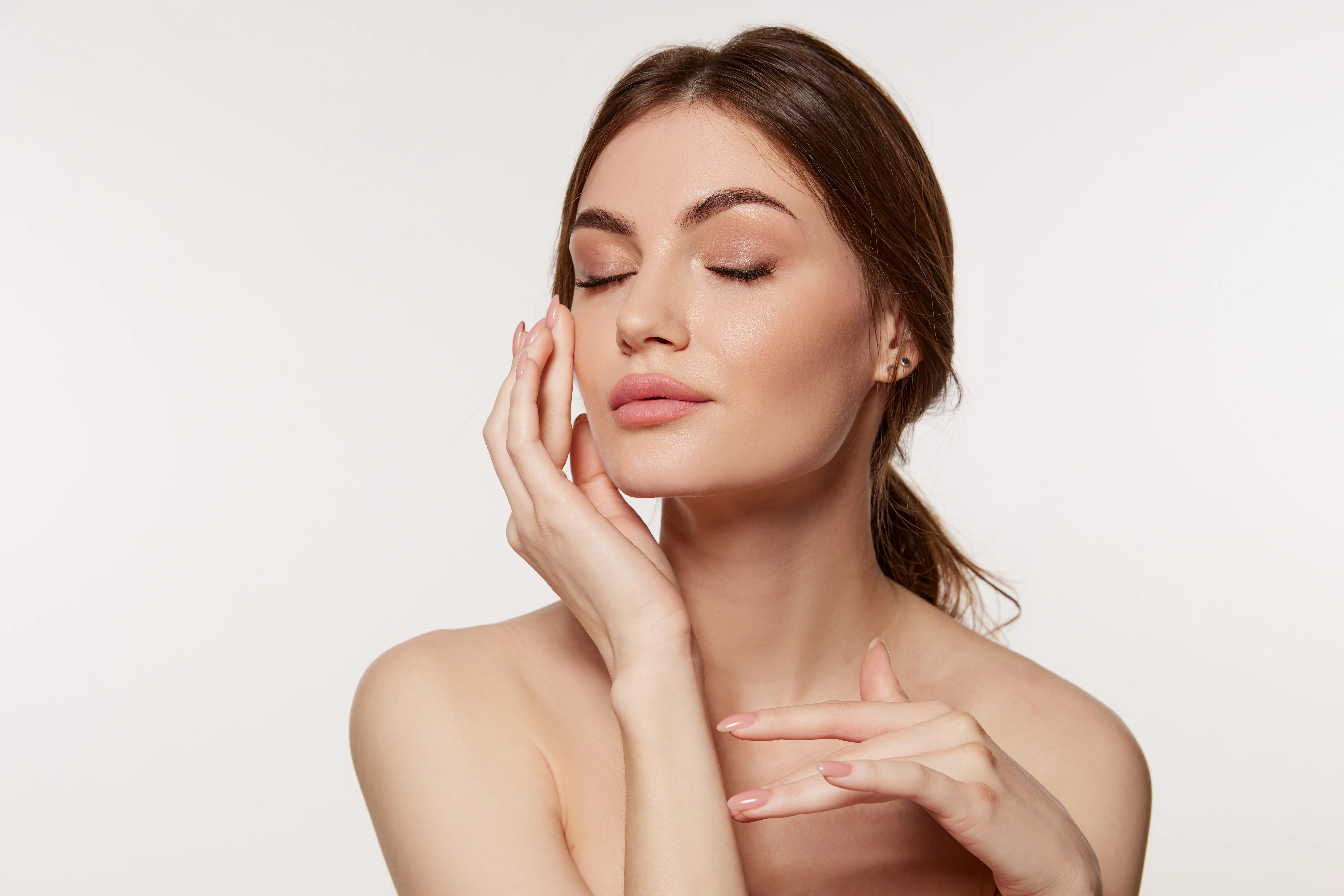 Woman with closed eyes gently touching her cheek against a light background