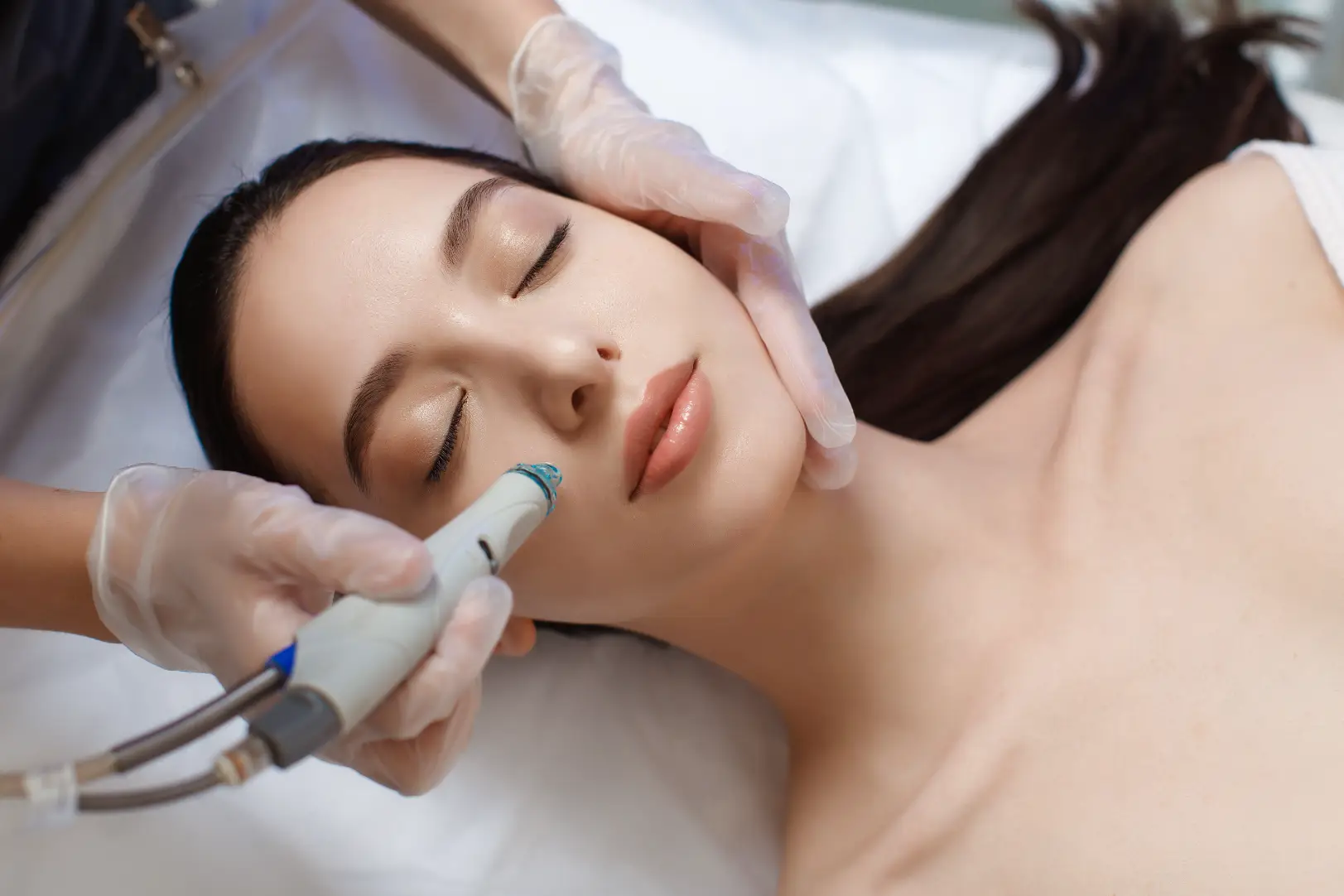 Provider using a facial treatment device on a reclining woman with eyes closed