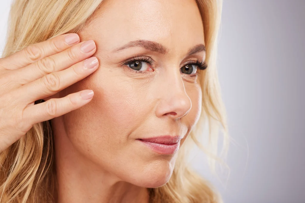 Close-up of a person touching the outer cheek near the eye with visible fine lines.
